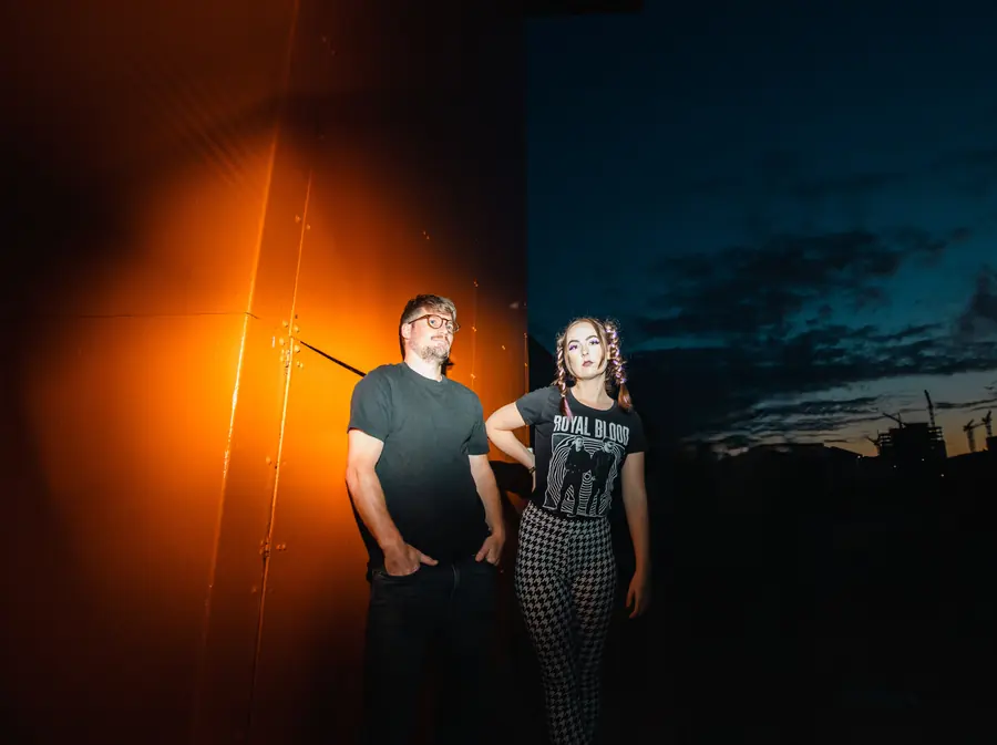Ronja Kaminsky and Nils Degenhardt of The Pinpricks in front of an orange wall at dusk